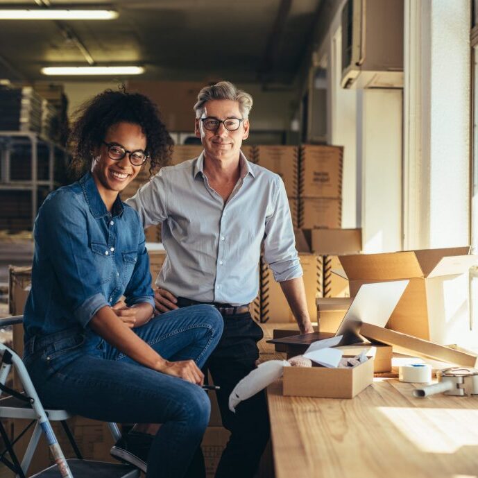Successful online shop business partners in a small office. Male and female entrepreneurs at their online shop warehouse looking at camera and smiling.
